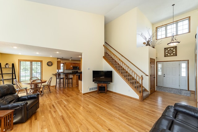 living area with a high ceiling, light wood-style flooring, and stairway