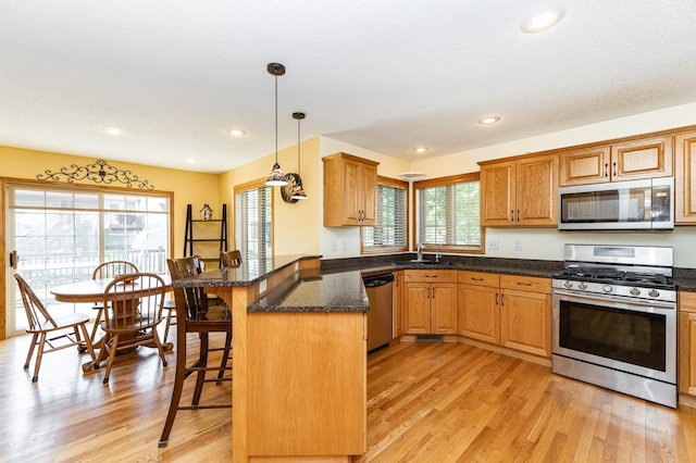 kitchen featuring stainless steel appliances, a sink, a peninsula, a breakfast bar area, and light wood-style floors