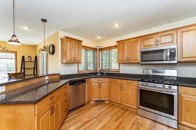 kitchen featuring stainless steel appliances, a sink, a textured ceiling, light wood-style floors, and a peninsula