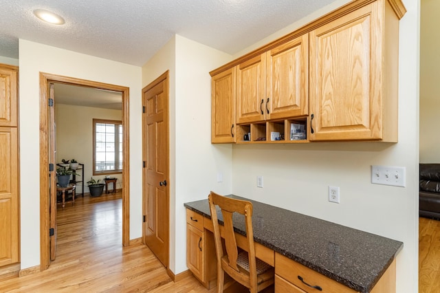 kitchen with light wood finished floors, dark stone counters, a textured ceiling, and baseboards