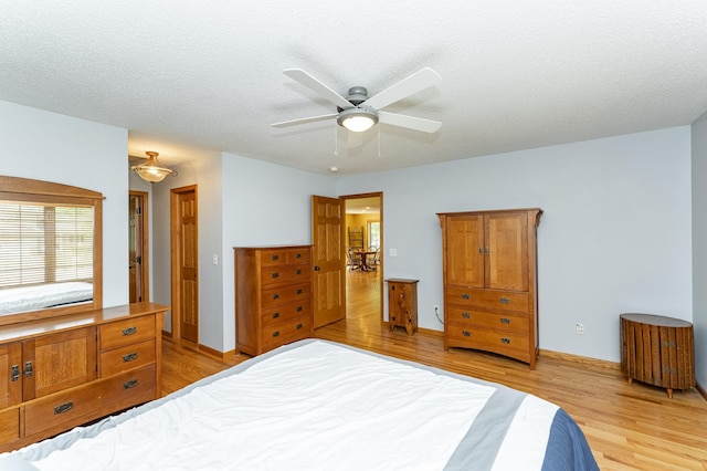 bedroom with light wood-type flooring, ceiling fan, baseboards, and a textured ceiling