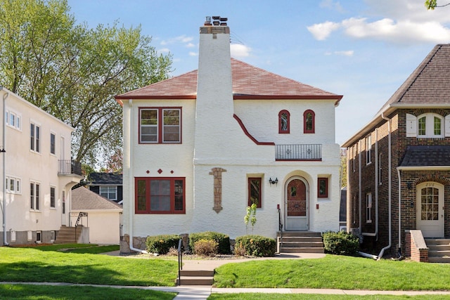 view of front of home featuring a chimney, a front yard, a balcony, and entry steps