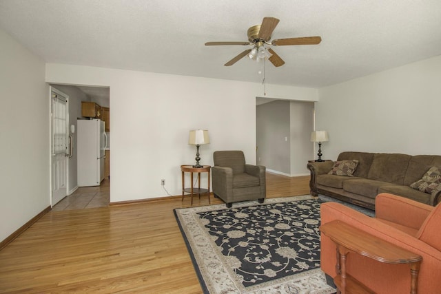 living room featuring ceiling fan, light wood-style flooring, and baseboards