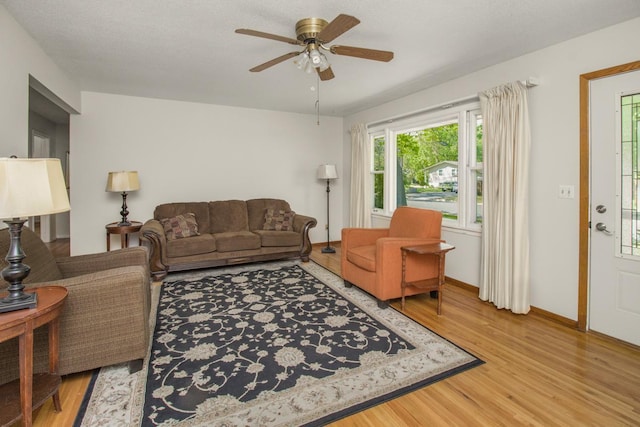 living area featuring light wood-style flooring, a ceiling fan, and baseboards