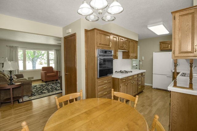 kitchen featuring white appliances, light wood-style flooring, decorative backsplash, a sink, and a chandelier