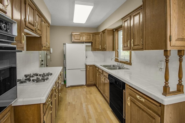 kitchen featuring a sink, white appliances, light wood-style floors, tasteful backsplash, and tile countertops