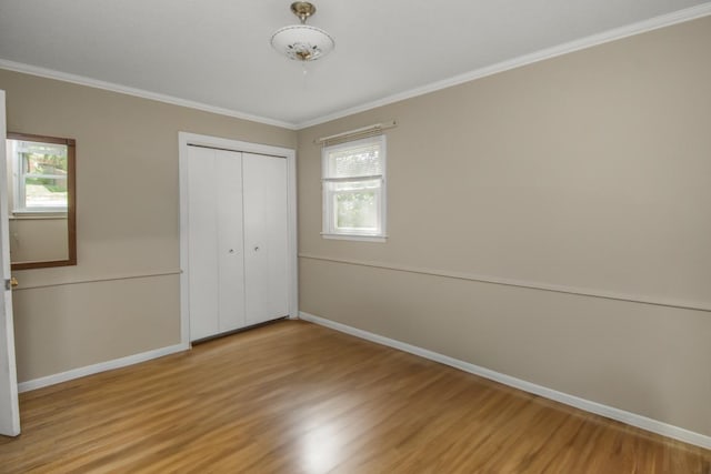unfurnished bedroom featuring light wood-type flooring, crown molding, baseboards, and a closet