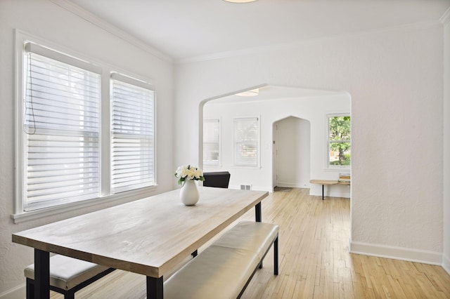 dining room with arched walkways, ornamental molding, light wood-style flooring, and baseboards
