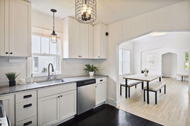 kitchen with stainless steel dishwasher, a sink, arched walkways, dark wood-style flooring, and light stone counters