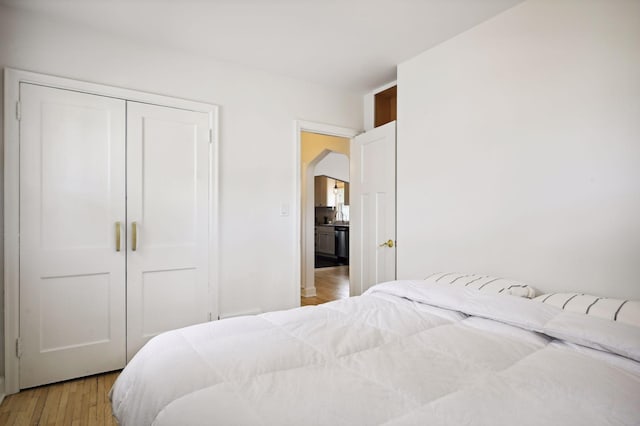 bedroom featuring arched walkways, light wood-type flooring, and a closet