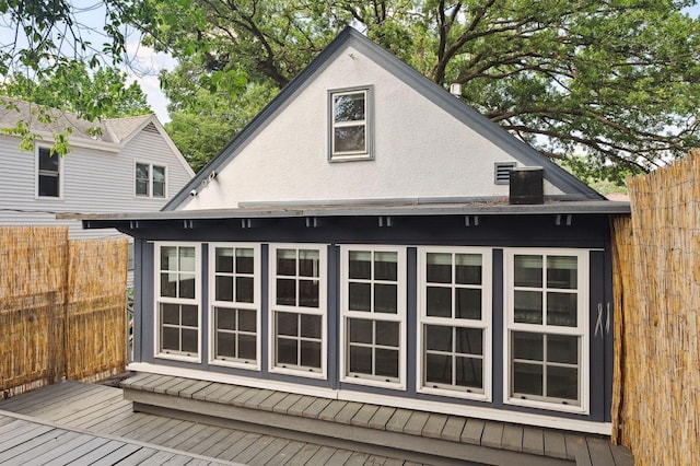 view of property exterior featuring stucco siding, a wooden deck, and fence