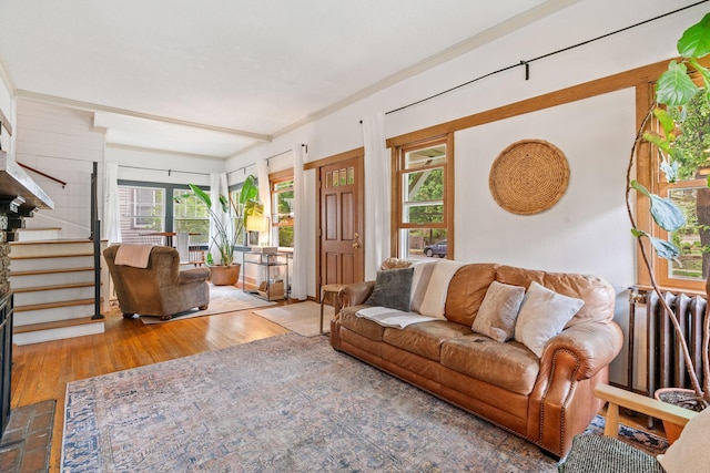 living area with radiator, wood finished floors, crown molding, and stairway