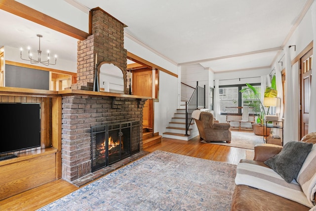 living room featuring wood finished floors, crown molding, a fireplace, stairs, and a chandelier