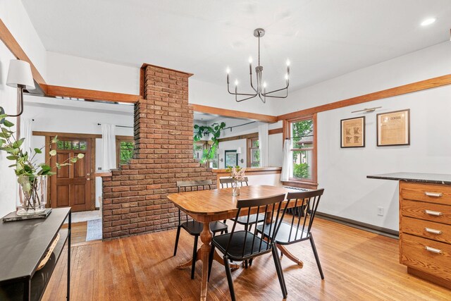 dining room featuring light wood finished floors, a chandelier, and brick wall