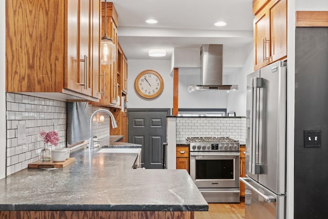 kitchen featuring high quality appliances, wall chimney range hood, a sink, decorative backsplash, and a peninsula