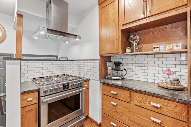 kitchen featuring stainless steel stove, wall chimney exhaust hood, backsplash, dark stone countertops, and open shelves