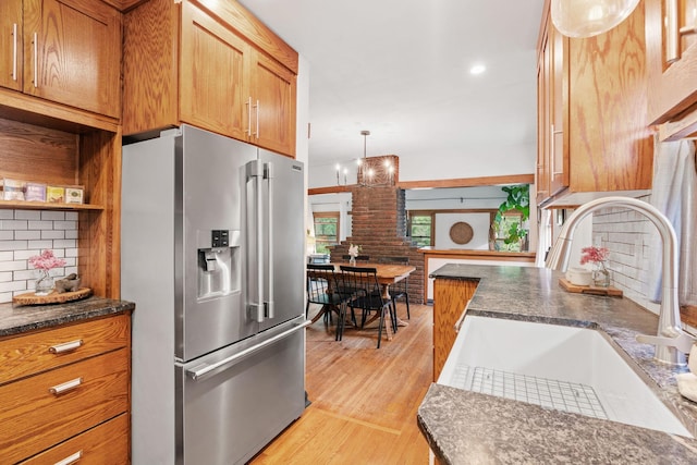 kitchen with high end refrigerator, a sink, backsplash, light wood-style floors, and hanging light fixtures