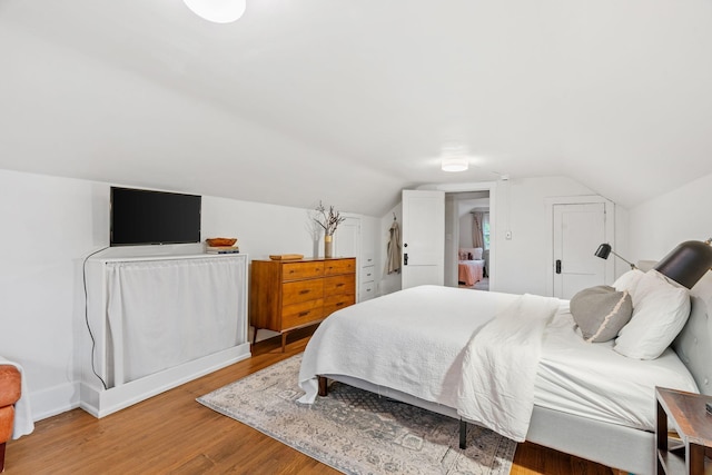bedroom featuring light wood-style flooring, lofted ceiling, and baseboards