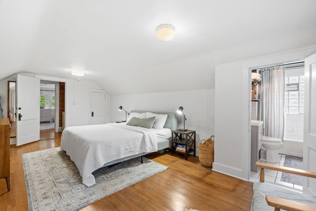 bedroom with ensuite bath, vaulted ceiling, wood finished floors, and baseboards