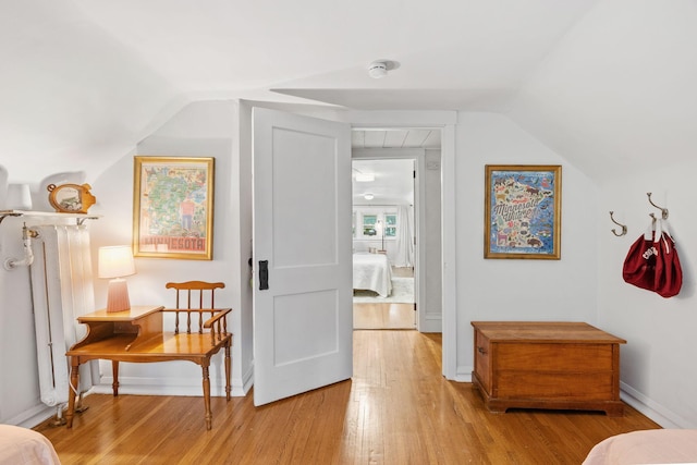 hallway featuring light wood-style floors, vaulted ceiling, and baseboards