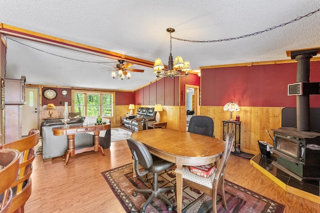 dining space with a wood stove, wood walls, wainscoting, a chandelier, and a textured ceiling