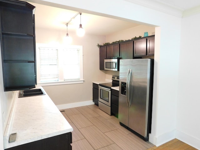kitchen with stainless steel appliances, track lighting, light countertops, dark brown cabinets, and a sink