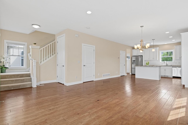 5024 Humboldt Ln N, Minneapolis, MN 55430 - unfurnished living room featuring a sink, a chandelier, light wood-style floors, stairs, and baseboards
