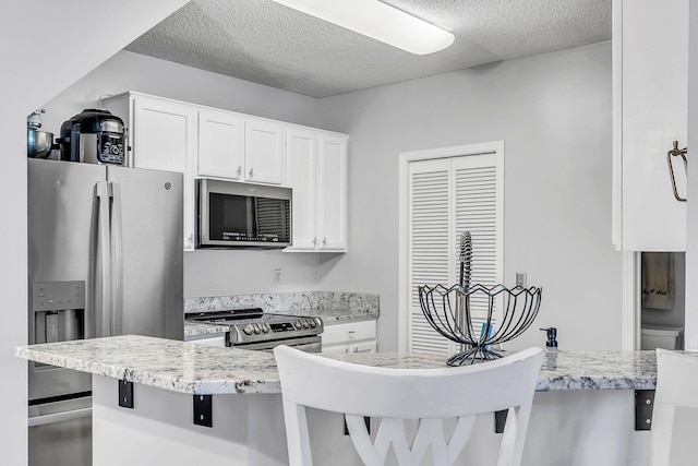1963 Bluestem Ln, Shoreview, MN 55126 - kitchen with stainless steel appliances, white cabinets, a textured ceiling, a kitchen bar, and light stone counters