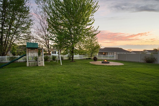 yard at dusk with an outdoor fire pit and a playground