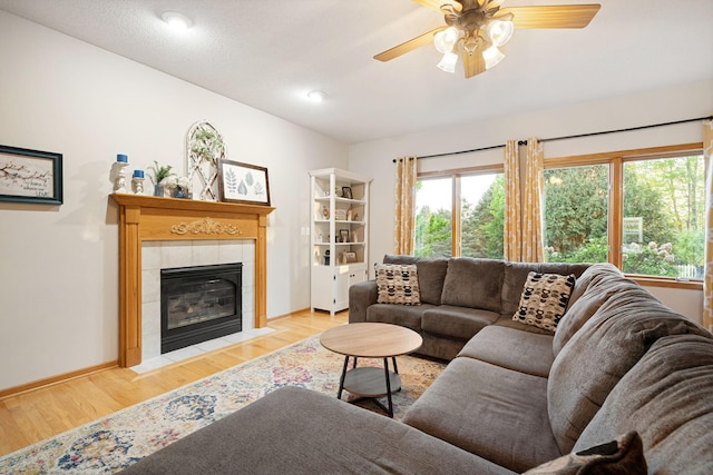living area with light wood finished floors, a tile fireplace, baseboards, and a ceiling fan
