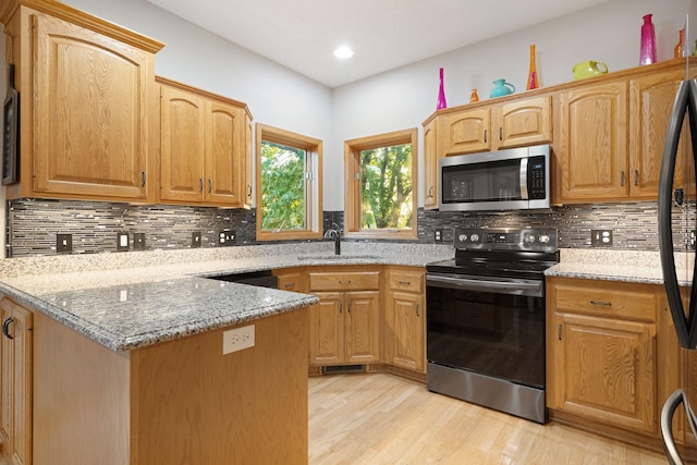 kitchen featuring stainless steel microwave, electric range oven, a sink, light wood finished floors, and light stone countertops