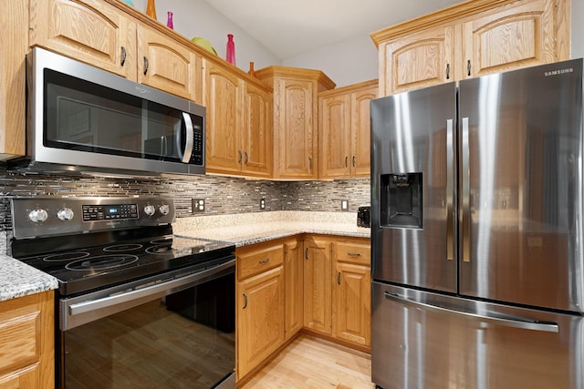 kitchen featuring stainless steel appliances, light stone counters, light wood finished floors, decorative backsplash, and light brown cabinets