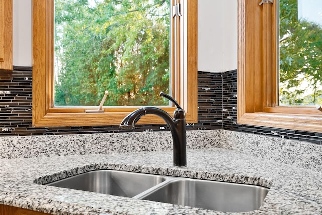 kitchen view of a sink, tasteful backsplash, and light stone countertops