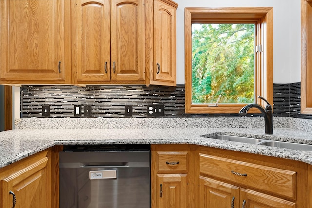 kitchen with a sink, dishwashing machine, backsplash, and light stone counters