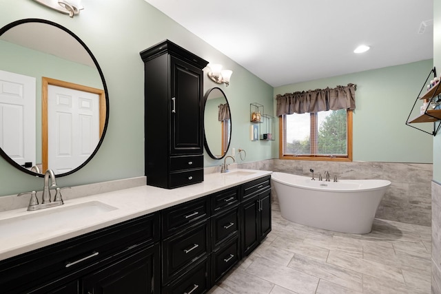 full bathroom with tile walls, wainscoting, a soaking tub, and double vanity