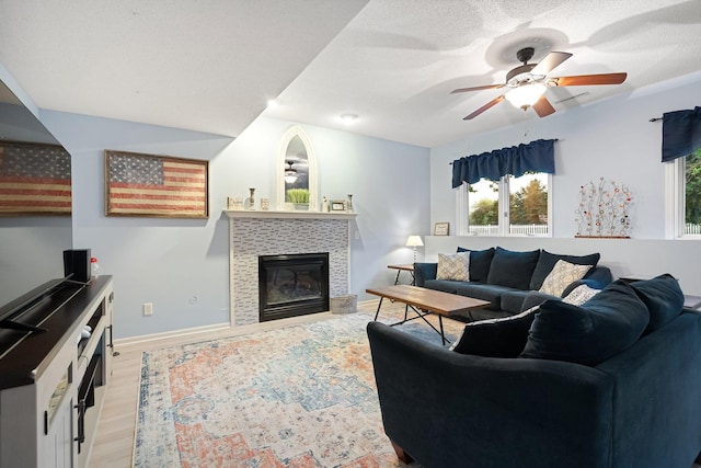 living area featuring ceiling fan, plenty of natural light, light wood-type flooring, and a fireplace