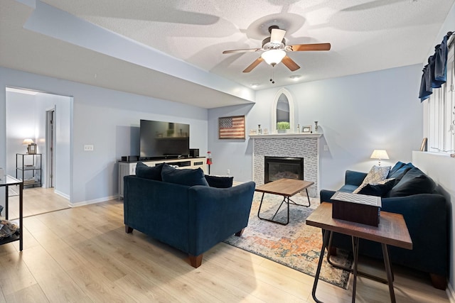 living area featuring a tile fireplace, a ceiling fan, light wood finished floors, baseboards, and a textured ceiling