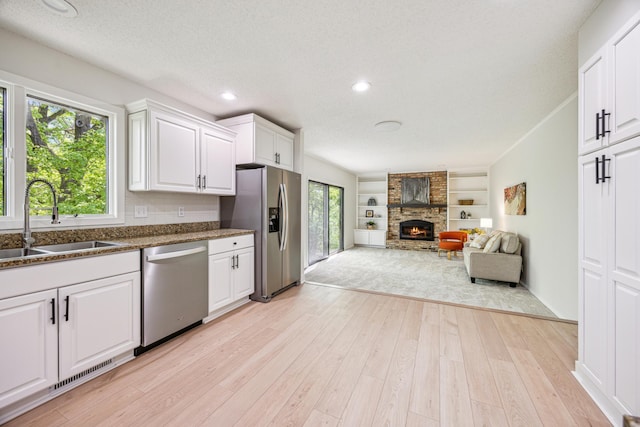 1588 Chatham Ave, Arden Hills, MN 55112 - kitchen featuring appliances with stainless steel finishes, a sink, a large fireplace, light wood-type flooring, and white cabinetry