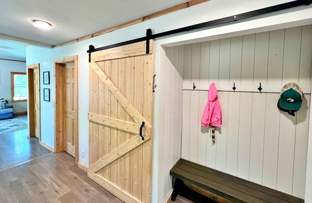 mudroom with wood finished floors, a barn door, wooden walls, and baseboards