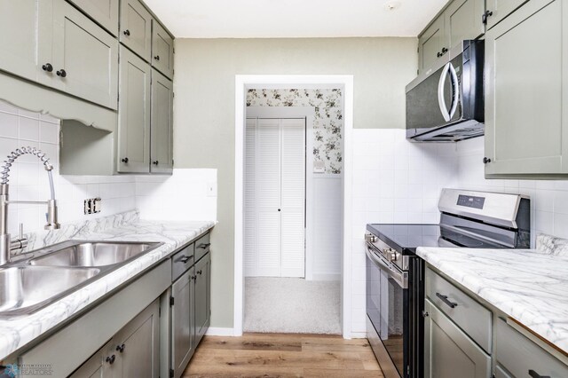 kitchen with stainless steel appliances, a sink, gray cabinetry, light wood-style flooring, and decorative backsplash