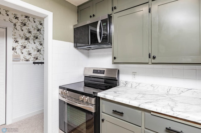 kitchen featuring appliances with stainless steel finishes, gray cabinets, wainscoting, light stone countertops, and wallpapered walls