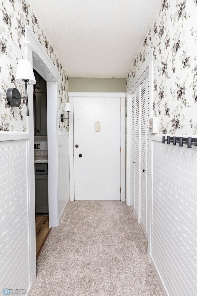 hallway featuring wallpapered walls, carpet floors, and wainscoting