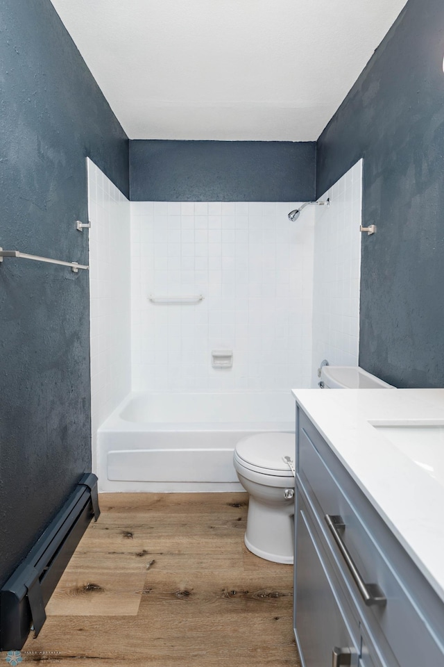 bathroom with wood finished floors, toilet,  shower combination, vanity, and a baseboard radiator