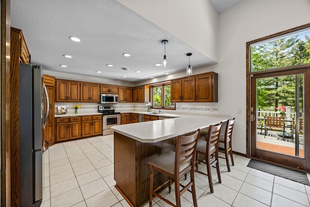 kitchen featuring appliances with stainless steel finishes, a peninsula, light tile patterned floors, light countertops, and brown cabinets