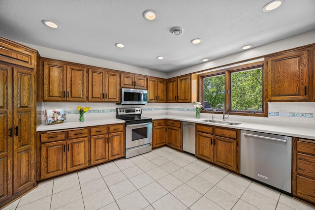 kitchen with stainless steel appliances, a sink, light countertops, decorative backsplash, and brown cabinetry
