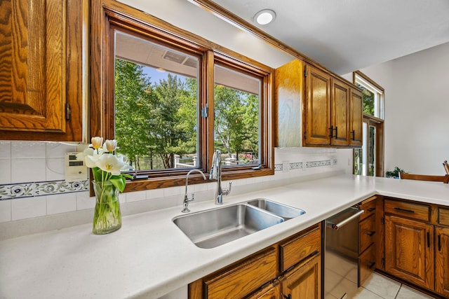 kitchen featuring dishwasher, a sink, light countertops, brown cabinets, and tasteful backsplash