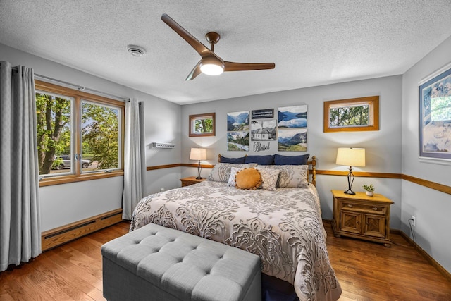 bedroom featuring a baseboard radiator, wood finished floors, a textured ceiling, baseboards, and a ceiling fan