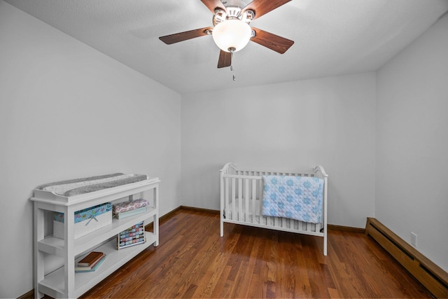 bedroom featuring a baseboard heating unit, wood finished floors, baseboards, and a ceiling fan