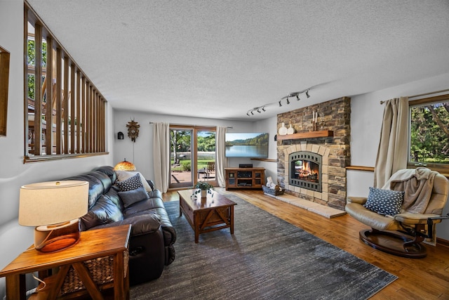 living area with a textured ceiling, plenty of natural light, hardwood / wood-style floors, a stone fireplace, and rail lighting