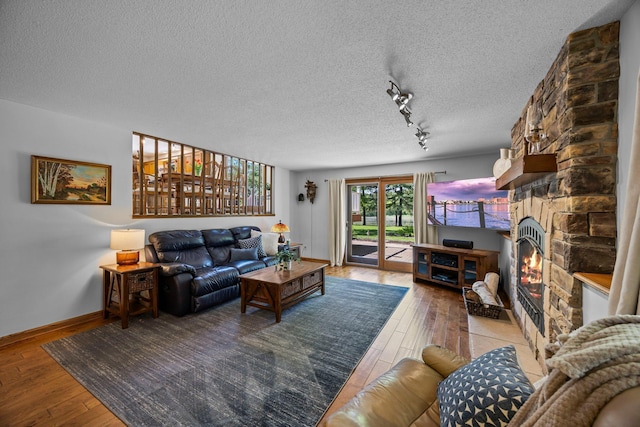 living room featuring hardwood / wood-style flooring, a textured ceiling, rail lighting, a stone fireplace, and baseboards